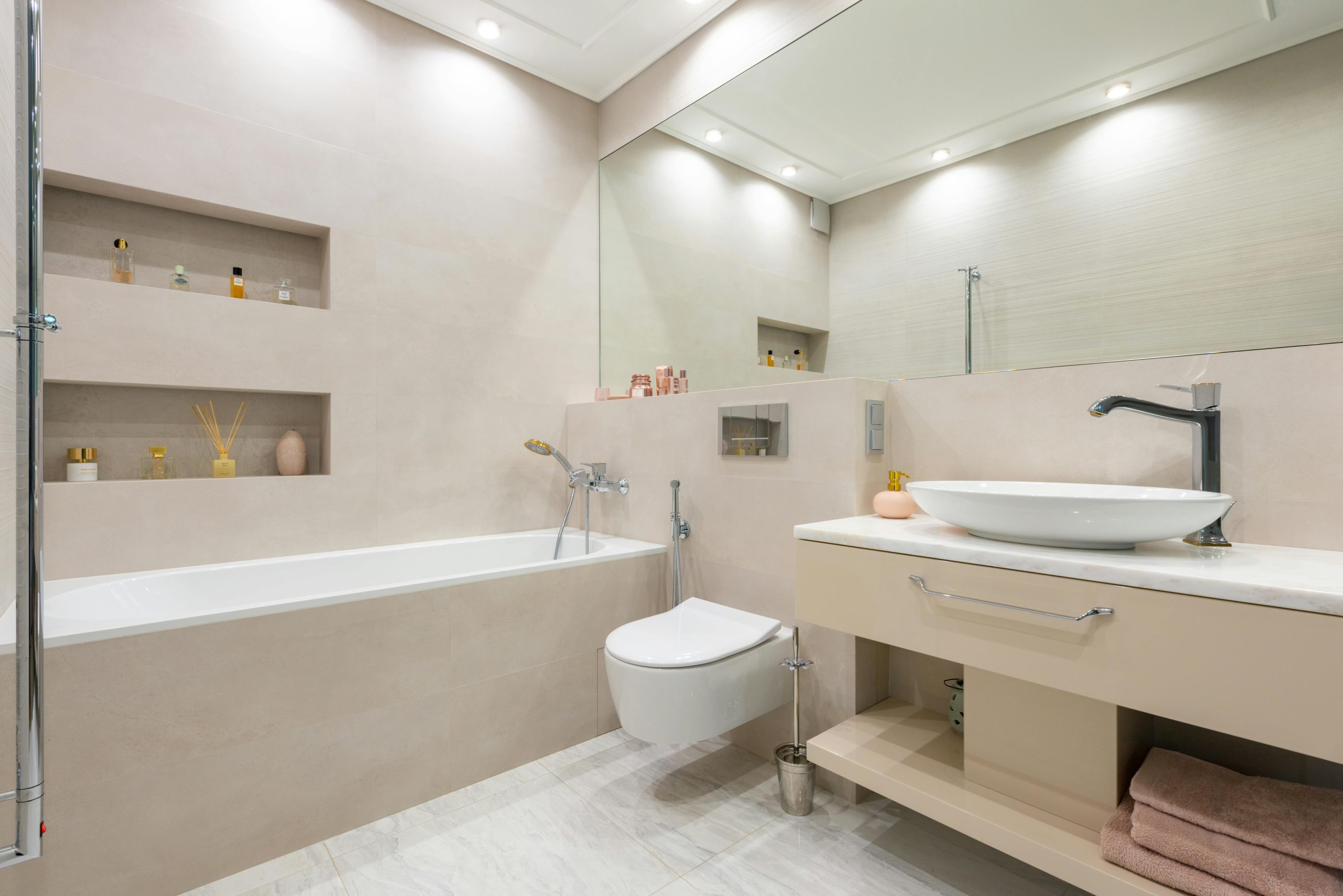 Interior of light modern bathroom with sink and faucet on cabinet with decorative objects next to bathtub and toilet under mirror and shelves